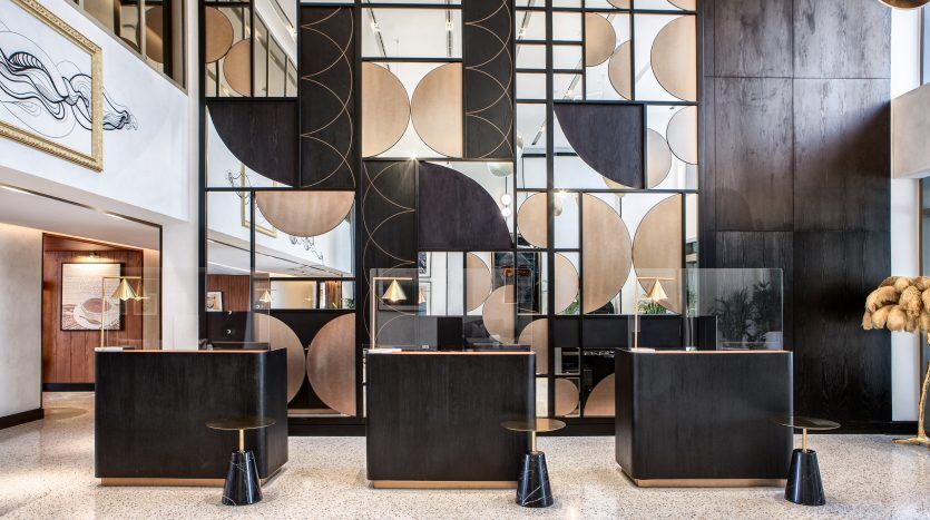 Hall d'entrée d'hôtel moderne avec deux comptoirs de réception géométriques noirs, un sol en damier et une grande cloison décorative aux motifs circulaires et semi-circulaires, rappelant le style sophistiqué de l'immobilier de Dubaï.