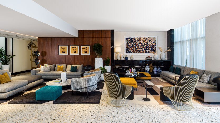 Salon moderne et spacieux dans une villa de Dubaï avec un mélange de meubles rayés et de couleur unie, de panneaux en bois, de grandes œuvres d'art au-dessus d'une cheminée noire et de grandes fenêtres.