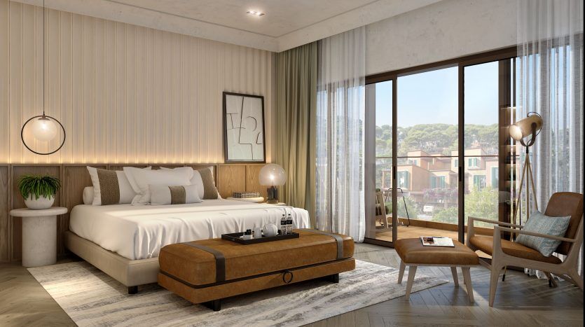 Une chambre moderne et ensoleillée dans un appartement de Dubaï avec un grand lit, des baies vitrées et des meubles élégants dont une chaise longue et une lampe de chevet décorative.