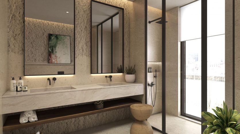 Une salle de bains élégante dans un appartement de Dubaï comprenant un long comptoir en pierre avec deux lavabos, de grands miroirs, des portes en verre à finitions noires menant à une douche, un panier tressé et un p