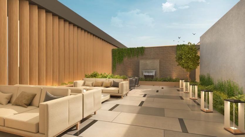 Un coin salon extérieur moderne dans une villa de Dubaï avec des canapés beiges, un mur en pierre avec cascade, des boiseries et des plantes vertes, sous un ciel dégagé.