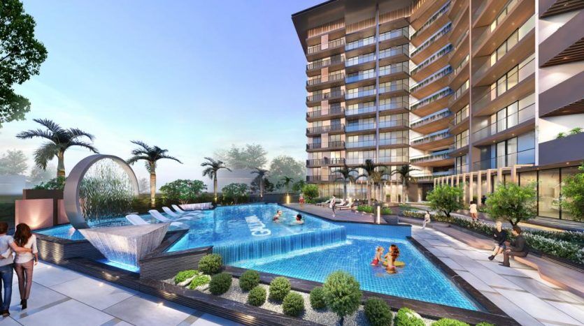 Un rendu artistique d'un immeuble d'appartements moderne à Dubaï comprenant une piscine extérieure avec des jeux d'eau, entourée d'espaces de détente et de verdure luxuriante, sous un ciel dégagé.