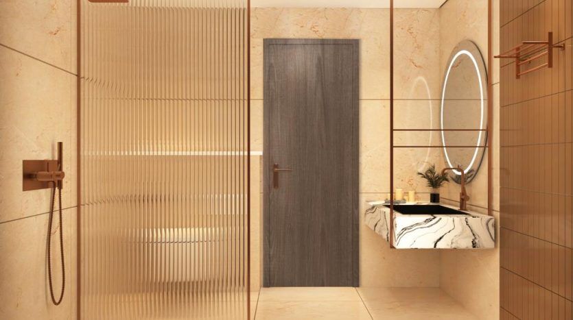Salle de bain moderne dans un appartement de Dubaï avec carrelage beige, comprenant une douche en verre, une porte en bois et une vasque avec un miroir circulaire éclairé par un éclairage LED.