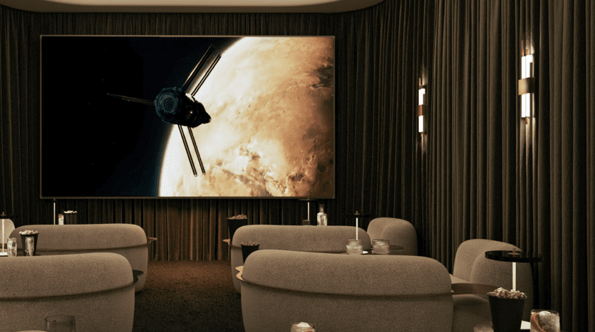 Une salle de cinéma maison luxueuse dans un appartement de Dubaï avec des murs et des rideaux sombres, dotée de grands sièges moelleux et d'un écran géant affichant une scène de vaisseau spatial. Un éclairage doux et des boissons créent une ambiance chaleureuse.