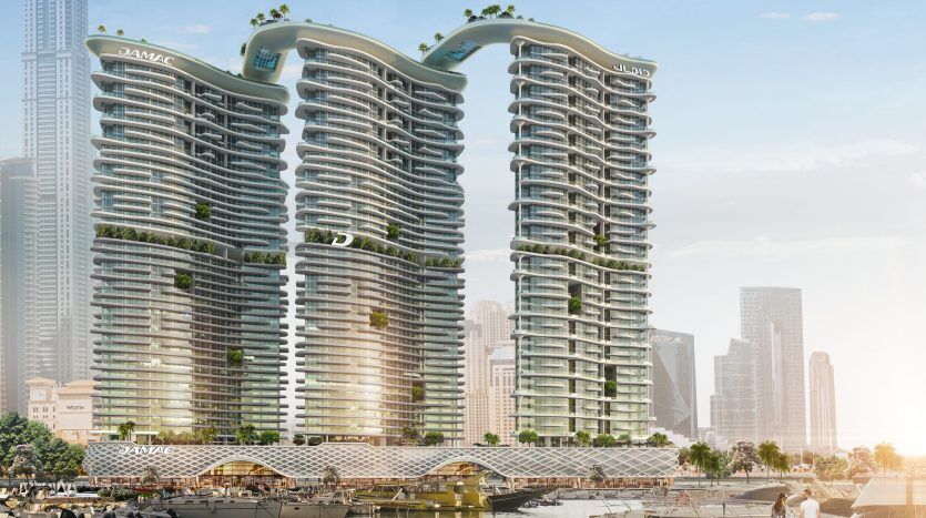 Deux gratte-ciel modernes aux courbes généreuses, avec une verdure abondante sur leurs balcons, surplombent un front de mer serein avec des bateaux, sur fond de paysage urbain de Dubaï sous un ciel brumeux.