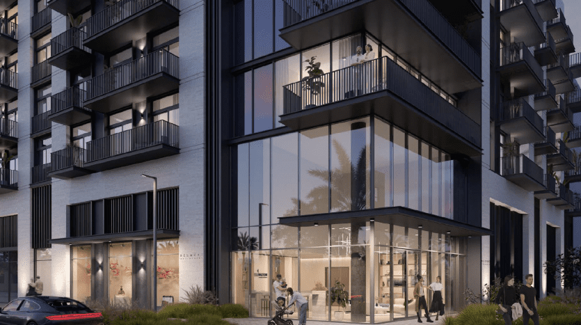 Immeuble d'appartements moderne à Dubaï au crépuscule avec des intérieurs éclairés, des balcons, un espace commercial au rez-de-chaussée et des piétons dont un cycliste et un couple marchant.