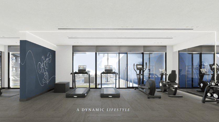 Une salle de sport spacieuse et moderne dans un appartement de Dubaï avec de grandes fenêtres offrant une vue sur la montagne. La salle dispose de tapis roulants, de vélos d'exercice et de machines elliptiques. Le sol est carrelé et il y a