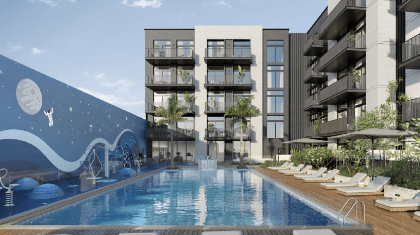 Un immeuble d'appartements moderne à Dubaï avec des balcons donnant sur une grande piscine flanquée de chaises longues sous un ciel bleu clair. Une fresque murale représentant une pieuvre sur un mur ajoute une touche ludique.
