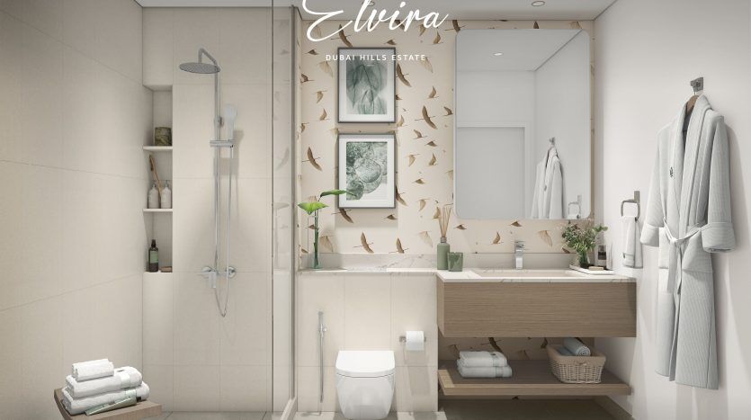 Intérieur de salle de bains moderne avec douche en verre, luminaires blancs, vanité en bois et décoré d'images végétales et d'autocollants d'oiseaux sur le mur. Le nom "Elvira" et le logo "Emaar" sont