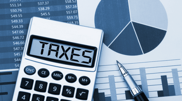 Calculatrice affichant les « taxes » sur son écran, avec un stylo, des graphiques à barres, un diagramme circulaire et des fiches de données financières sur l'investissement Dubaï en arrière-plan, représentant l'analyse financière ou le calcul des impôts.