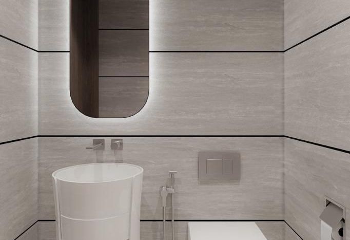 Salle de bains moderne et minimaliste avec des carreaux beige neutre, comprenant un miroir ovale unique, un lavabo rond suspendu avec un socle cylindrique et des toilettes blanches élégantes. Éléments de décoration minimalistes visibles dans cette villa Dubaï