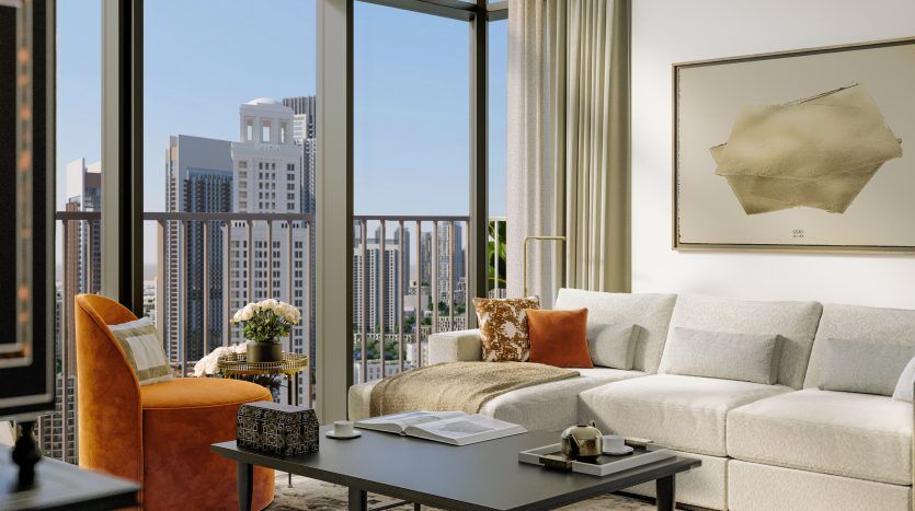 Salon moderne dans un appartement de Dubaï avec de grandes fenêtres montrant les toits de la ville, comprenant un canapé blanc, une chaise orange et une table basse. La pièce affiche une décoration minimaliste et élégante.