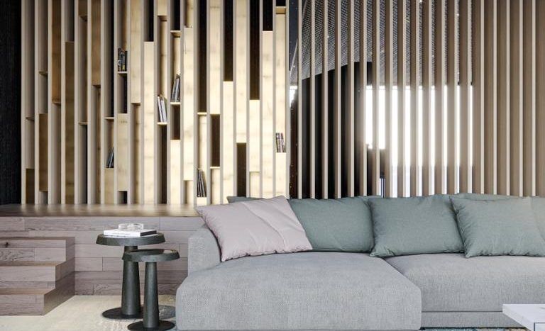Un salon moderne dans un appartement de Dubaï comprenant un grand canapé sectionnel gris, un tapis artistique multicolore et des murs à lattes verticales en bois. La pièce comprend un effet de plafond de nuit étoilée unique