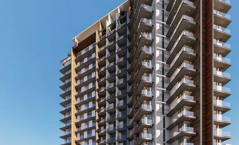 Un immeuble résidentiel moderne de grande hauteur avec de grands balcons, entouré de palmiers, sous un ciel bleu clair. Au premier plan, une voiture jaune passe et une personne prend une photo. Cette scène