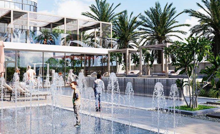 Des enfants jouent dans une fontaine extérieure moderne dans un complexe de luxe à Dubaï, entourés de palmiers et de façades architecturales élégantes sous un ciel bleu clair.