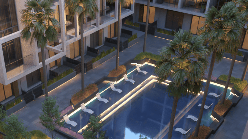 Une image nocturne sereine d'une villa de luxe à Dubaï avec une piscine éclairée entourée de palmiers et de chaises longues, flanquée de bâtiments à plusieurs étages.