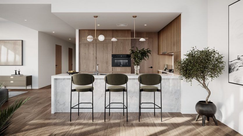 Intérieur de cuisine moderne comprenant un îlot en marbre avec trois tabourets de bar verts, des armoires en bois, des appareils électroménagers intégrés et un élégant arbre en pot. Les tons neutres et les lignes épurées créent un look élégant adapté à un appart