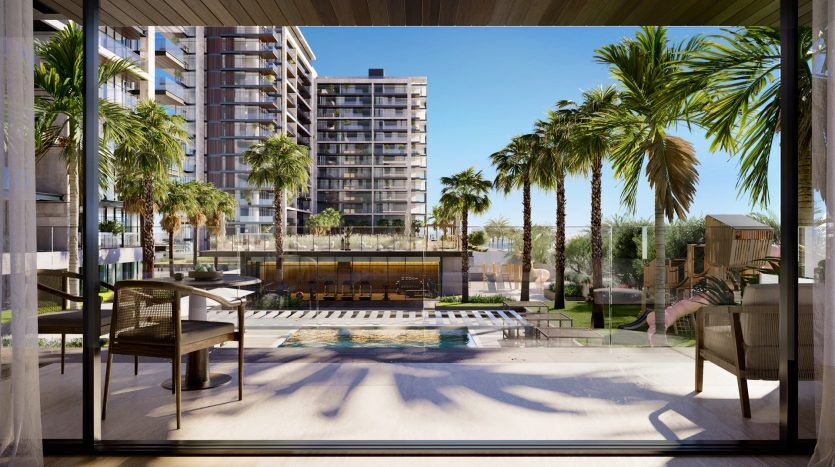 Vue depuis une terrasse moderne donnant sur une piscine luxueuse avec des palmiers et des immeubles d'habitation de grande hauteur à Dubaï, sous un ciel bleu clair.