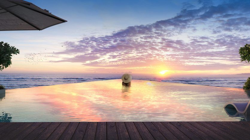 Une personne portant un chapeau de soleil profite d'un coucher de soleil serein depuis une piscine à débordement dans une villa à Dubaï, avec des oiseaux volant au loin et des plantes à proximité.