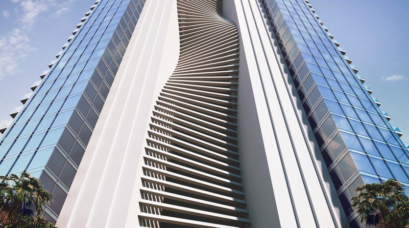 Gratte-ciel futuriste avec une façade ondulée unique, dominant un ciel bleu clair, entouré d'une verdure luxuriante à sa base à Dubaï.