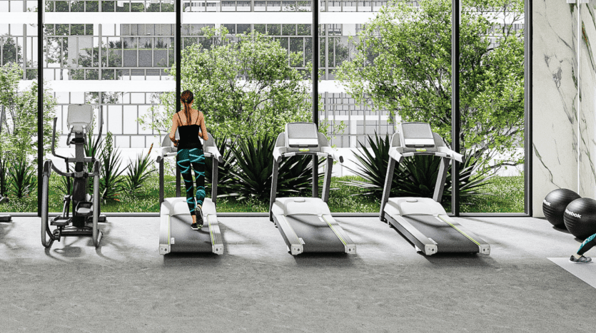 Une femme utilisant un tapis roulant dans une salle de sport moderne avec de grandes fenêtres donnant sur un feuillage vert, à côté d'autres équipements de fitness et un ballon de stabilité dans une villa de Dubaï.