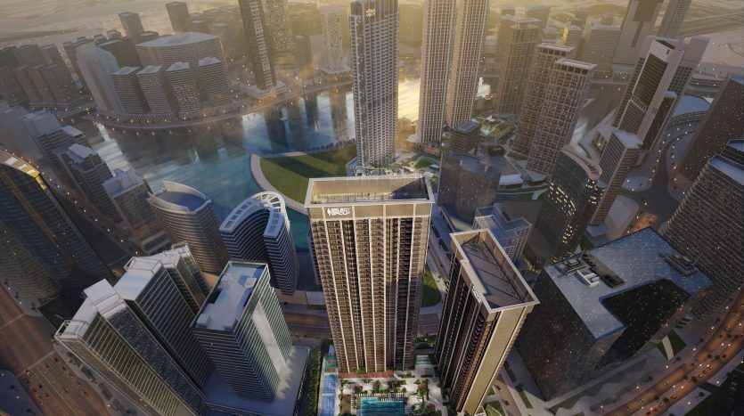 Vue aérienne d'un paysage urbain moderne de Dubaï au crépuscule, avec un gratte-ciel important avec une piscine sur le toit, entouré de nombreux autres immeubles de grande hauteur et de rues éclairées.