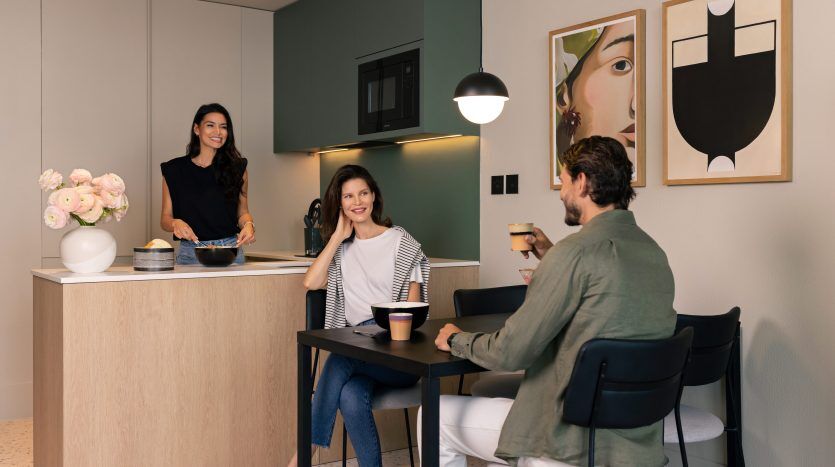 Trois personnes profitent d’une conversation informelle dans une cuisine moderne d’une villa à Dubaï. Une femme prépare à manger au comptoir, tandis qu'une femme et un homme assis discutent à une table à manger.