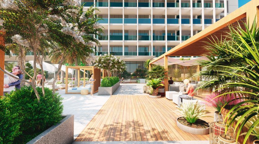 Une terrasse extérieure animée d'un hôtel de luxe à Dubaï, avec une verdure luxuriante, des allées en bois et des clients profitant de leur temps libre sous un ciel ensoleillé.