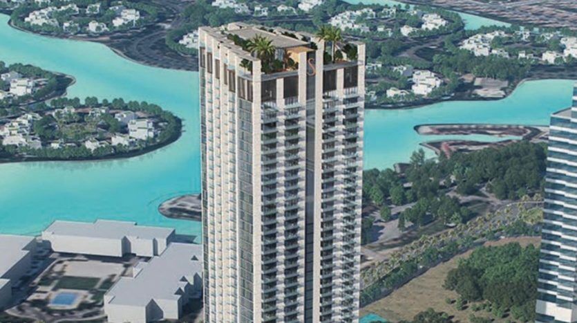 Vue aérienne d'un grand gratte-ciel avec une verdure luxuriante sur le toit, entouré d'un réseau de plans d'eau turquoise et d'un feuillage dense dans un cadre urbain à Dubaï.