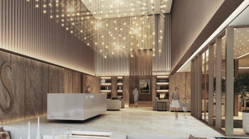 Un hall d'entrée opulent avec un grand lustre, des sièges luxueux, des sols en marbre et une palette de couleurs neutres soulignées par un éclairage tamisé met en valeur le luxe qui rappelle l'immobilier haut de gamme de Dubaï.