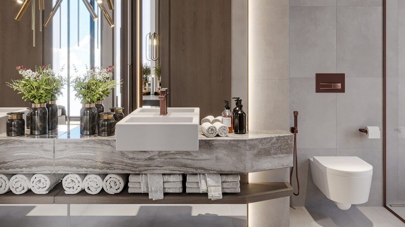 Salle de bains moderne dans une villa de Dubaï comprenant un comptoir en marbre avec un lavabo rectangulaire blanc, plusieurs serviettes blanches soigneusement disposées, des articles de toilette assortis et des compositions florales éclatantes sous un grand miroir.