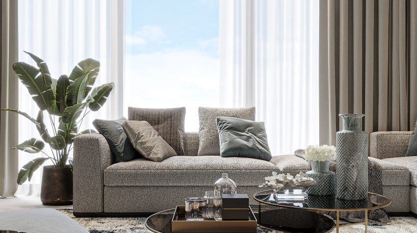 Salon élégant comprenant un canapé gris moderne avec des coussins, des tables basses rondes en verre, de grandes fenêtres avec des rideaux transparents, un tapis à motifs bleus et une plante d'intérieur. Des suspensions élégantes sont suspendues au-dessus