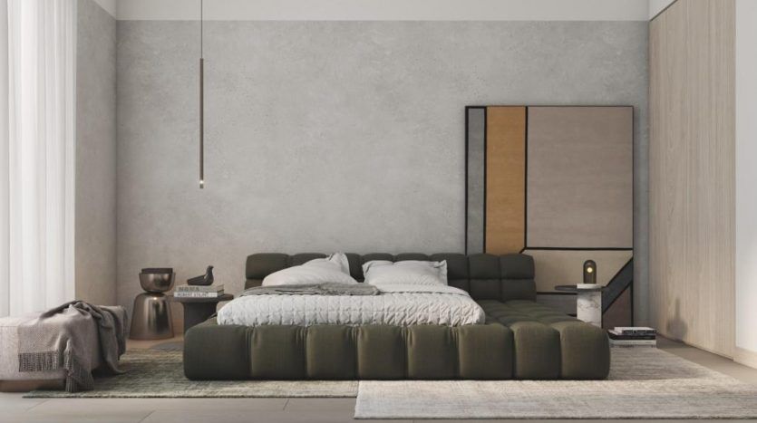 Une chambre minimaliste dans un appartement de Dubaï comprenant un grand lit vert avec un jeté texturé, une table d'appoint avec des livres, une lampe et une grande peinture abstraite au-dessus du lit. La chambre est une salle de bain
