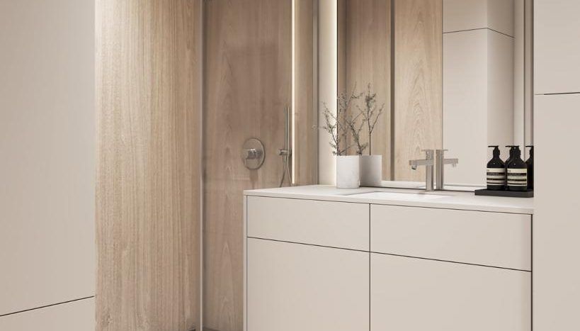 Une salle de bain moderne avec des armoires en bois, un lavabo blanc et une cabine de douche en verre. Le décor subtil comprend un vase de fleurs et des bouteilles noires minimalistes. Les tons clairs dominent l'espace de cette villa Dubaï.