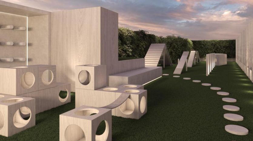 Aire de jeux extérieure moderne avec structures de jeu géométriques, découpes circulaires et tremplins sur gazon artificiel, sous un ciel sombre à proximité d'une agence immobilière de Dubaï.