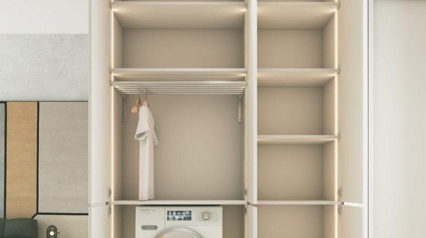 Une armoire intégrée moderne dotée d'étagères ouvertes et d'une section avec une machine à laver en bas, le tout dans un thème beige doux assorti à l'intérieur de l'appartement à Dubaï.