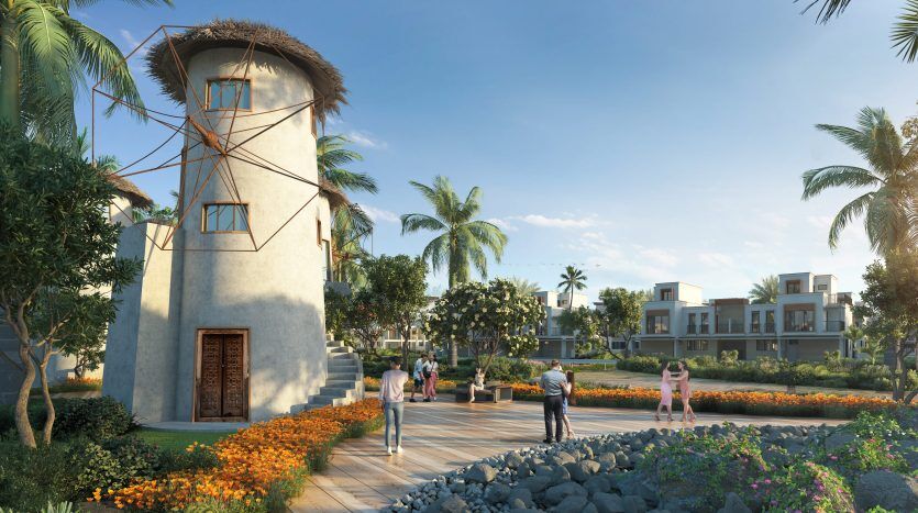 Un cadre communautaire pittoresque à Dubaï avec des gens marchant près d'un bâtiment cylindrique unique entouré de jardins luxuriants, de palmiers et de maisons modernes sous un ciel bleu clair.