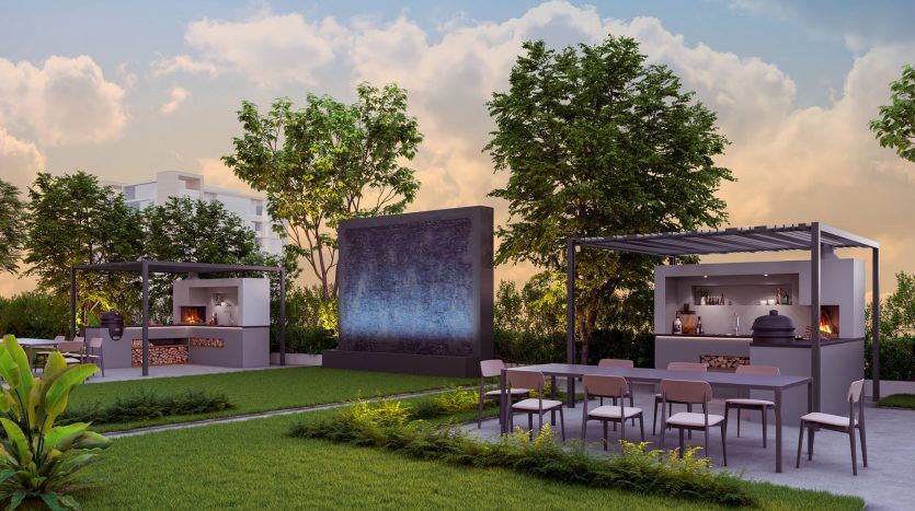 Une configuration de cinéma en plein air avec un grand écran entouré de verdure et un espace bar moderne avec tabourets et tables, situé dans un jardin luxuriant au crépuscule à Dubaï.