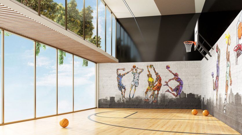 Un terrain de basket intérieur lumineux avec de grandes fenêtres et une fresque murale représentant des joueurs de basket colorés et abstraits. Un cerceau est monté sur un mur ; des ballons de basket sont éparpillés sur le parquet d'un quartier privilégié de Dubaï