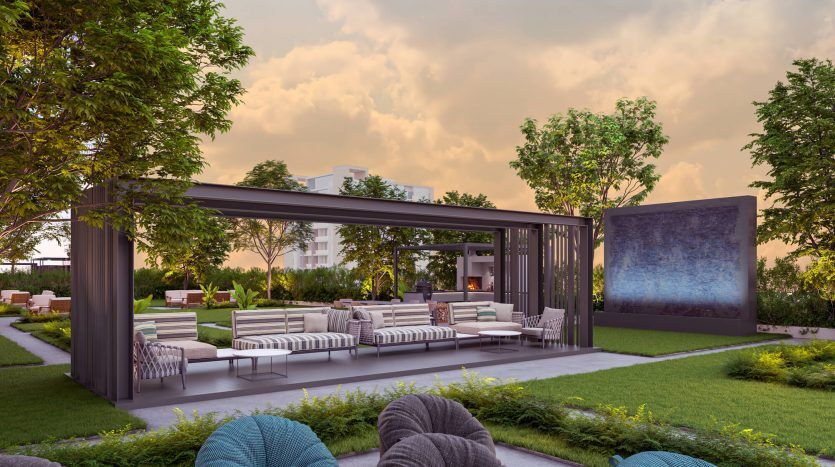 Un espace de vie extérieur moderne comprenant une pergola minimaliste avec des sièges confortables, une verdure luxuriante et un panneau décoratif surdimensionné ; sur un ciel de coucher de soleil dans une luxueuse villa à Dubaï.