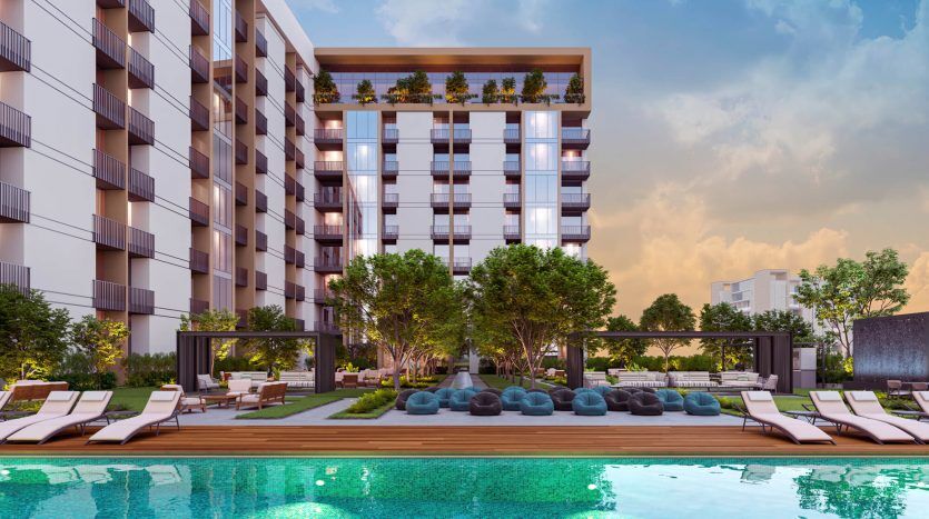 Immeuble d'appartements moderne à Dubaï avec balcons donnant sur la piscine et doté de chaises longues, de kiosques et de sièges luxueux au milieu d'un aménagement paysager luxuriant au crépuscule.