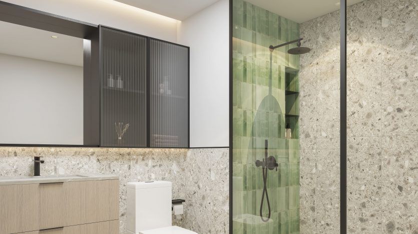 Salle de bains moderne dans une villa de Dubaï comprenant une cabine de douche en verre sans cadre avec un mur de carrelage vert, des toilettes blanches et une vanité en bois contre un mur en pierre texturée. Design lumineux et épuré.