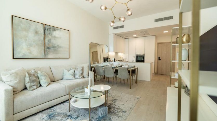 Un salon moderne dans une villa de Dubaï avec un canapé beige, des chaises assorties, une table basse ronde blanche et un grand tableau abstrait. La pièce s'ouvre sur un coin repas avec une table dressée pour