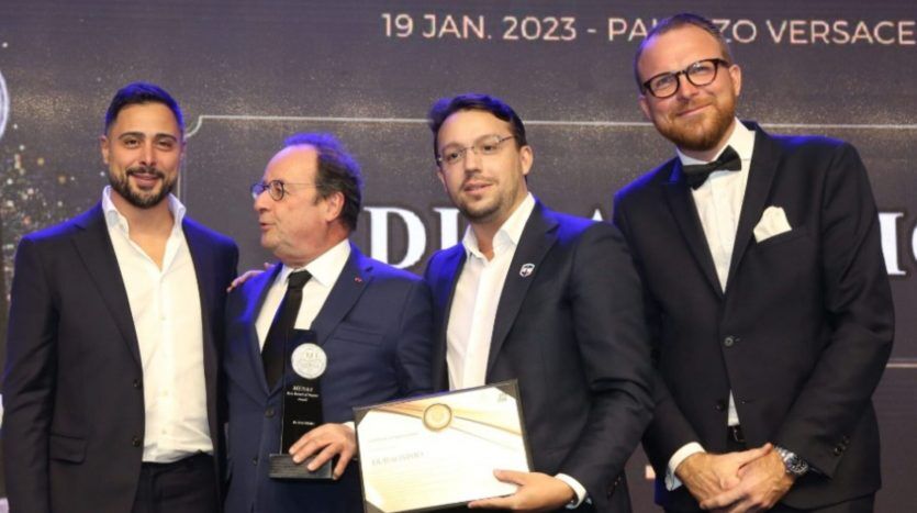 Quatre hommes vêtus de tenues formelles, souriants, posant lors d'une cérémonie de remise de prix d'investissement à Dubaï. L'un est titulaire d'un certificat de récompense. Une bannière en arrière-plan affiche la date de l'événement, "19 janvier.