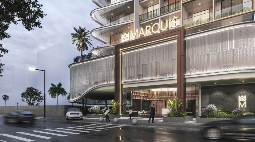 Vue extérieure du bâtiment marquis au crépuscule, présentant un design moderne avec une architecture incurvée et une signalisation lumineuse, entouré de palmiers et d'une rue de la ville avec des voitures et des piétons à Dubaï.