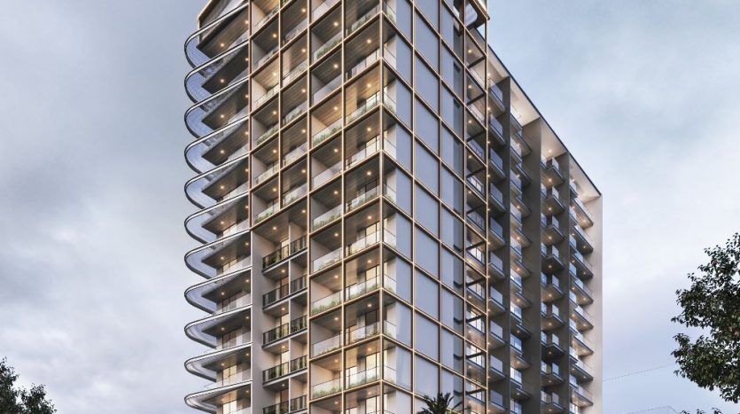 Un immeuble moderne de grande hauteur à Dubaï illuminé le soir, doté de vastes façades et balcons en verre, avec une scène de rue animée comprenant des véhicules flous et des palmiers.