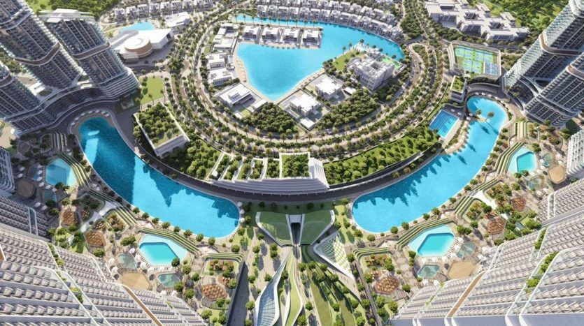 Aerial view of a modern, futuristic urban landscape with skyscrapers surrounding a central artificial lagoon with turquoise waters, linked by bridges and landscaped with lush greenery, including exclusive villas at