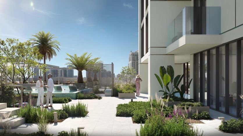 Elegant urban garden in Dubai with people walking among palm trees and modern buildings, with paved paths, greenery and a distant skyline under a clear sky.