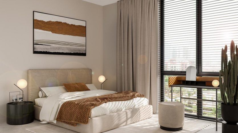A modern bedroom in a Dubai villa with a beige upholstered bed, white bedding, a brown throw, a desk by the window, lamps, a large plant and a framed abstract painting.