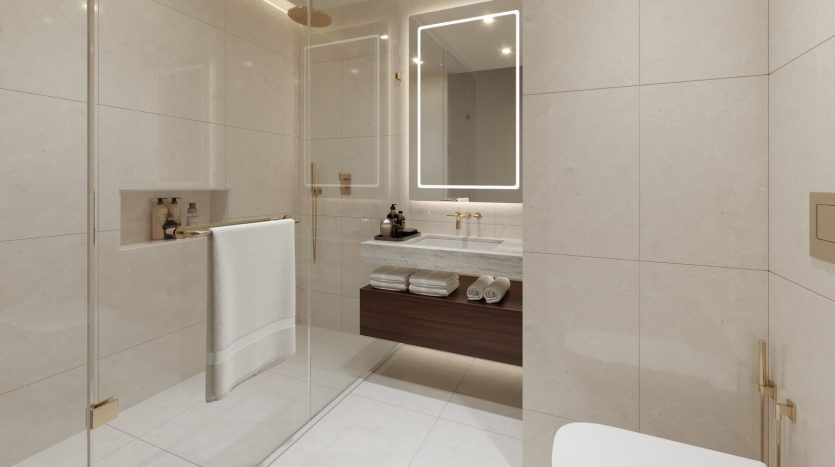 Une salle de bains moderne dans une villa de Dubaï comprenant une douche en verre, un grand miroir au-dessus d'une vanité en bois avec lavabo et des toilettes blanches. Les murs et le sol sont carrelés en beige clair.